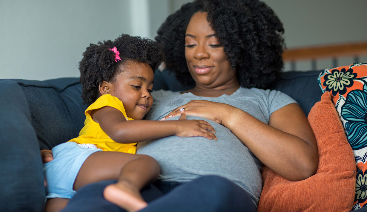 Pregnant mother and daughter together on couch