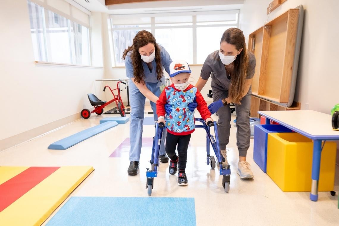 child being assisted by nurses and walking device