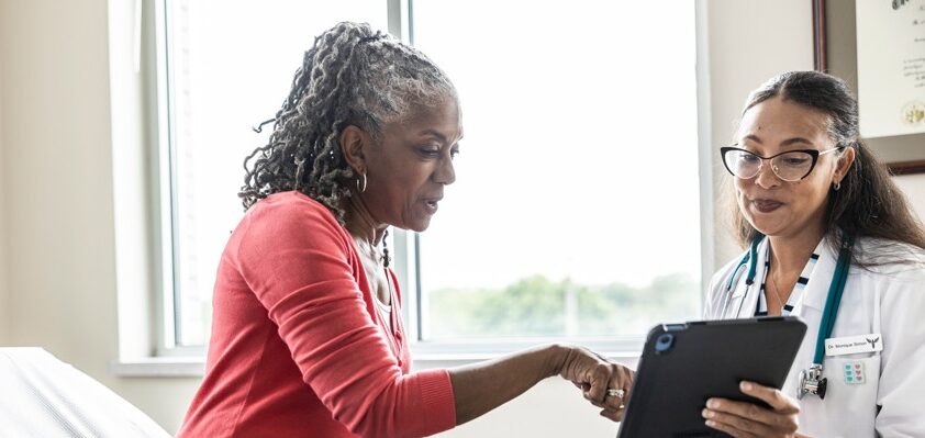 Female doctor and senior woman looking at digital tablet in exam room