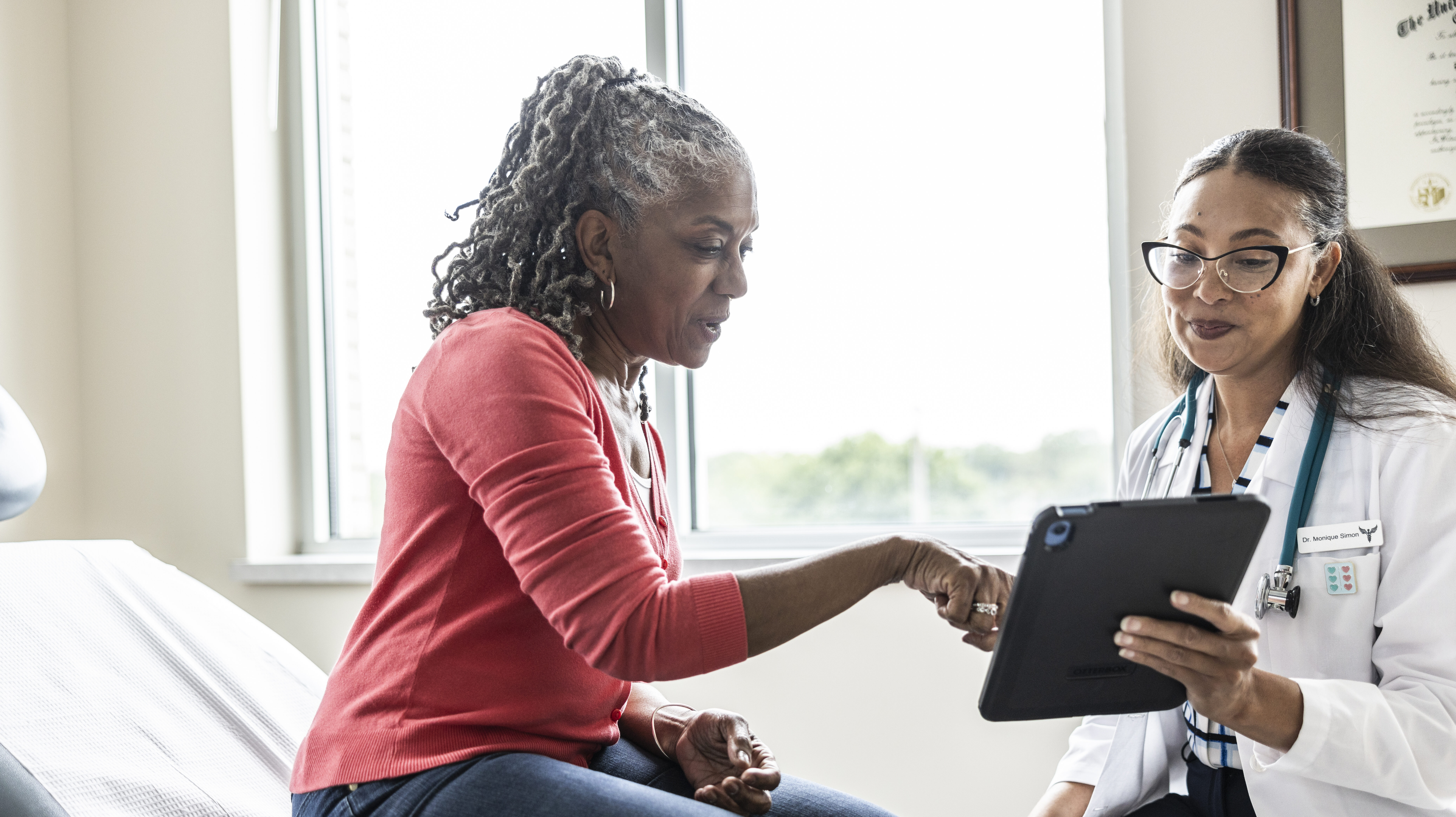 Female doctor and senior woman looking at digital tablet in exam room