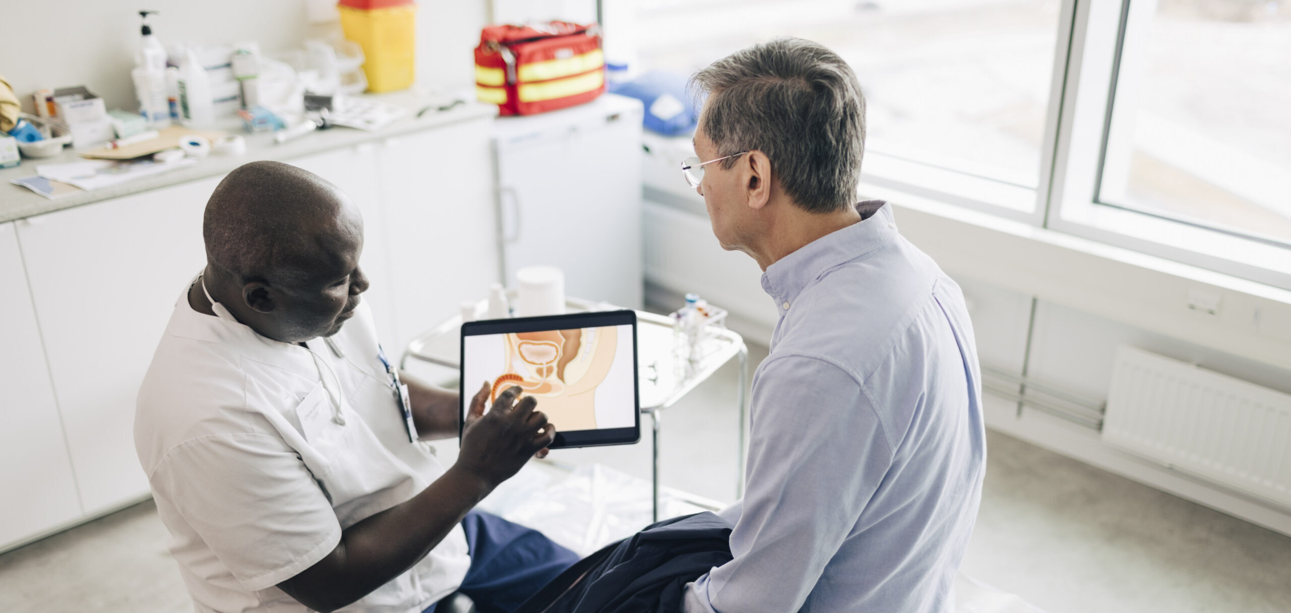 Prostate Cancer Screening: What the PSA Test Can and Can’t Tell You High angle view of doctor discussing male reproductive system with patient on digital tablet while sitting in medical ro