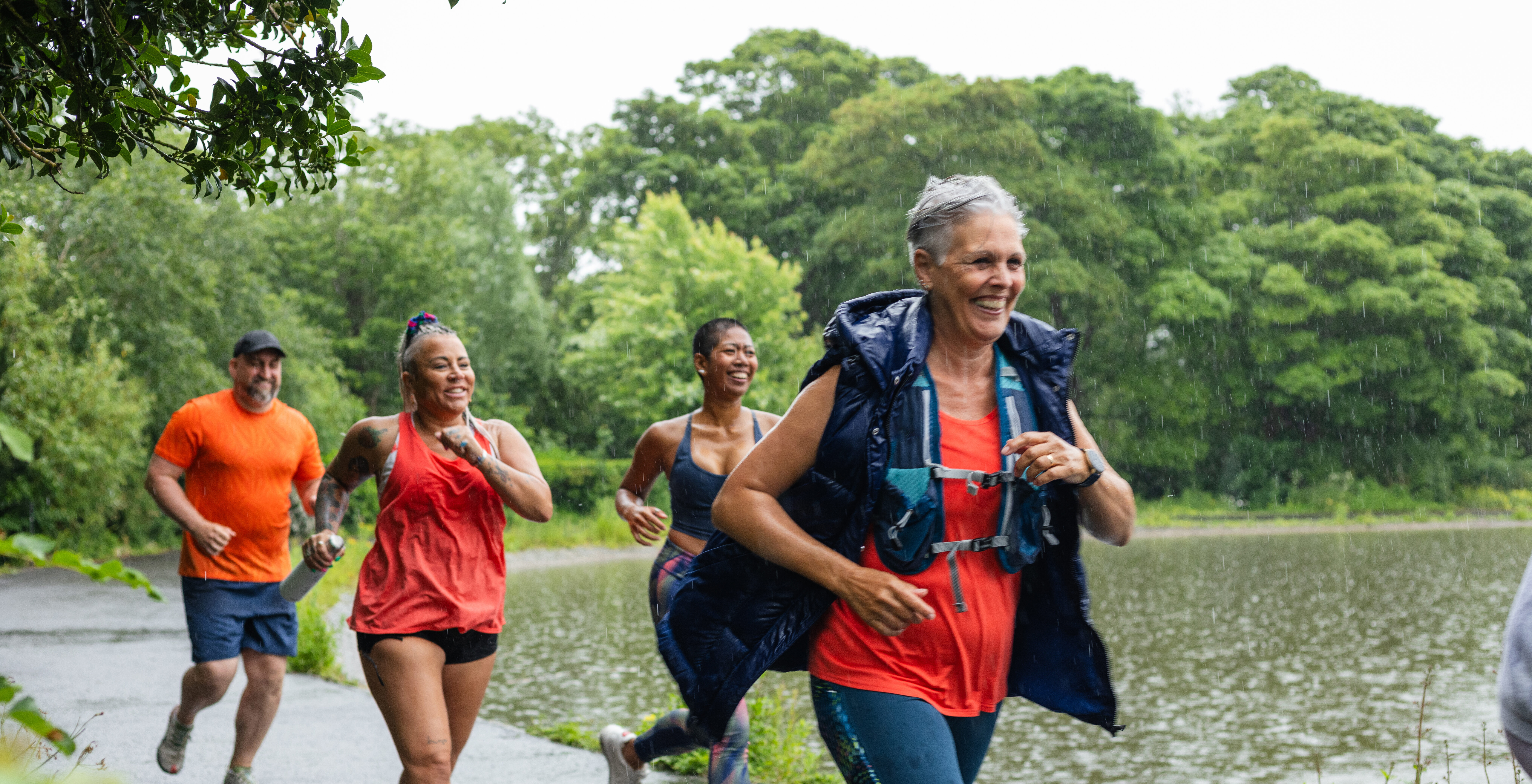 Runners taking part in a community fun run in the rain in Leazes Park in Newcastle upon Tyne, North East England. They are smiling as they run and follow each other on a path. The race is open to people of all ages and abilities and is also dog friendly. These files have similar videos/images available.