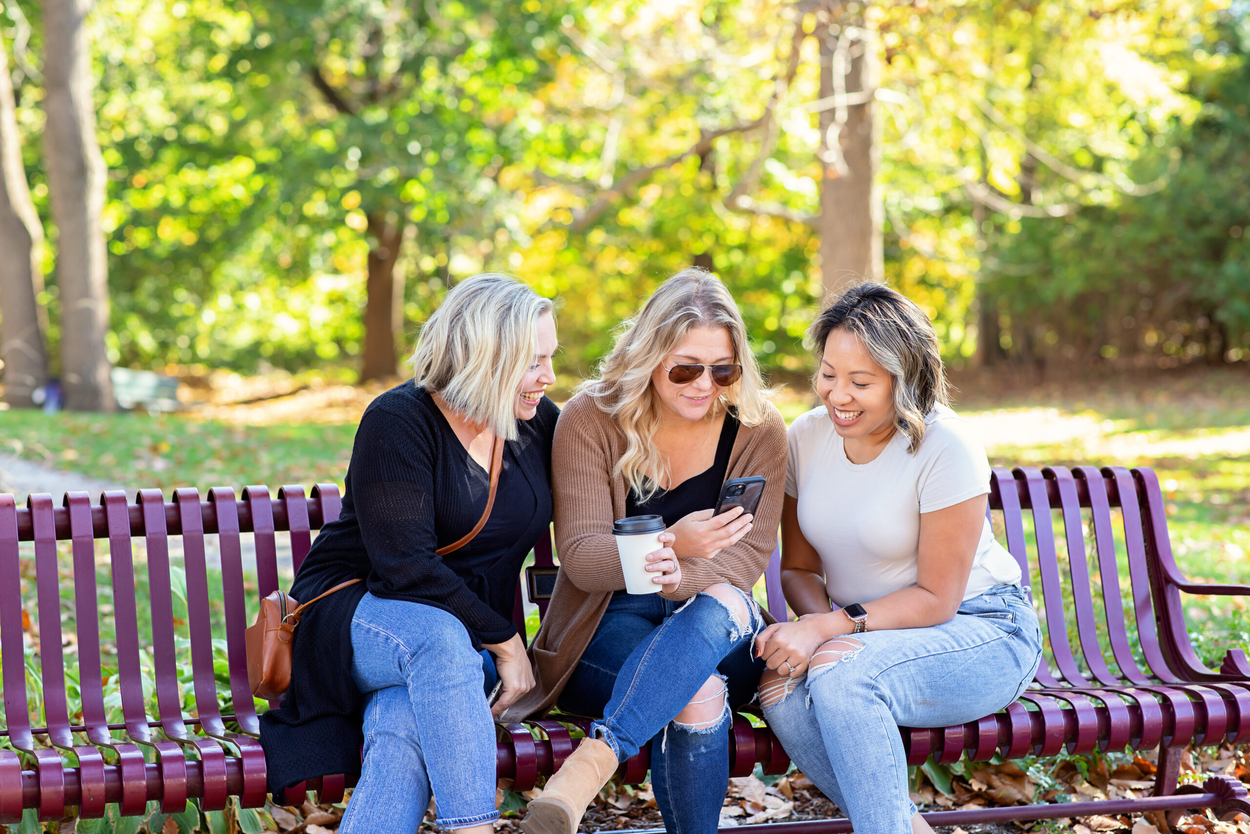 Three women sitting on a bench looking at a friend's phone